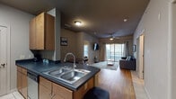 This single-floor unit offers a thoughtfully designed layout that balances comfort and functionality. The galley-style kitchen is equipped with stainless steel appliances, including a full-size refrigerator, stove, and dishwasher, complemented by warm wood cabinetry and dark countertops. A double-basin sink anchors the kitchen peninsula, which opens directly into the living area for a seamless flow.

The living room is bright and welcoming, featuring wood-style flooring, a ceiling fan, and a set of sliding glass doors that lead to a private balcony overlooking an outdoor view. Decorative framed artwork adds a touch of character to the neutral-toned walls.

The unit includes two bedrooms, each with wood-style flooring and ceiling fans. The primary bedroom benefits from multiple windows that allow natural light to fill the space, while both rooms offer a calm, restful atmosphere.

The bathroom is finished with tile flooring, dark countertops, warm wood cabinetry, and a shower-tub combination. A walk-in closet is accessible directly from the bathroom, providing generous storage.

Overall, the unit presents a cohesive, modern aesthetic with a neutral color palette and practical finishes throughout.