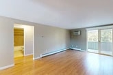 Located at 59 State St in Tully, NY, this 2-bedroom, 1-bathroom unit offers a practical and comfortable single-floor layout. The living room is a bright, open space finished with light hardwood flooring, neutral-toned walls, and a sliding glass door that opens to a private balcony with views of surrounding greenery. Baseboard heating and a wall-mounted air conditioning unit ensure year-round comfort. The galley-style kitchen is efficiently designed with warm honey-toned wood cabinetry, granite-look countertops, and black appliances including a refrigerator, electric range, and microwave. A stainless steel sink and ample cabinet storage add to its functionality. An adjacent dining nook features a pendant light fixture and a window that brings in natural light. The full bathroom is finished with warm beige floor tiles and a tiled tub-surround with a decorative mosaic accent strip, complemented by a wood-toned vanity. Both bedrooms feature plush carpeting and neutral walls, offering a quiet retreat. A dedicated closet and connecting hallways complete the layout, providing practical storage and circulation throughout the space.