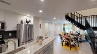 This two-story residence in Houston, TX (77090) offers a well-designed layout across two floors, blending functional living spaces with contemporary finishes throughout. The main level centers around an open-concept kitchen and dining area, where white shaker cabinetry, granite countertops, a dark tile backsplash, and stainless steel appliances—including a French door refrigerator and electric range—create a polished, practical cooking space. A granite-topped island with an undermount sink provides additional workspace and casual seating. A sliding barn door adds a distinctive architectural touch, leading to a conveniently located half bathroom. The adjacent dining area accommodates a full-sized table, while the living room features recessed lighting, a ceiling fan, large windows with neighborhood views, and ample space for comfortable seating. Upstairs, the primary bedroom includes French doors opening to a private balcony, hardwood-style flooring, and an en suite bathroom with granite vanity and walk-in closet access. Additional bedrooms are well-proportioned with hardwood-style floors and bright, neutral walls. The home's clean white palette and recessed lighting throughout contribute to a bright, welcoming ambiance on both levels.