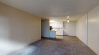This single-floor unit offers a functional and straightforward layout designed for comfortable everyday living. The open-concept living area is finished with plush carpet flooring and neutral-toned walls, creating a clean and versatile space. Textured ceilings are consistent throughout, and ceiling-mounted light fixtures provide ambient illumination. The living area flows naturally toward the kitchen, which is set apart by hardwood-style vinyl flooring. The kitchen features white cabinetry extending to the upper walls for ample storage, a peninsula with a white countertop that doubles as a prep and serving surface, a double-basin sink, and black appliances including a refrigerator, dishwasher, and range with an overhead ventilation hood. A dedicated bedroom includes carpeted flooring, a window that allows natural light to filter in, and a baseboard heating unit. The entry area also benefits from natural light through a window, contributing to the overall brightness of the unit. The space is designed with practicality in mind, offering a cohesive flow between the living, kitchen, and sleeping areas, making it well-suited for straightforward, day-to-day functionality.