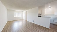 Located at 17301 Keelson Ln in Huntington Beach, California, this single-floor unit offers a thoughtfully arranged layout that makes efficient use of its space. The open-concept living and kitchen area forms the heart of the unit, bathed in natural light from a large window fitted with vertical blinds. The living area features light wood-look flooring and a textured ceiling, lending a clean and airy feel throughout.

The kitchen is designed with functionality in mind, featuring white cabinetry that extends to the upper walls for ample storage, a light stone-effect countertop, a built-in range with exhaust hood, a stainless steel refrigerator, and a single-basin sink. A peninsula with vertical shiplap paneling separates the kitchen from the living space, adding a subtle design detail while maintaining an open flow.

The unit includes two bathrooms, each finished in a consistent, neutral palette. One bathroom features a full tub-shower combination with a bright transom window above, while the other showcases a white vanity with a stone-topped counter, a large mirror, and built-in storage cabinetry. Both bathrooms continue the light wood-look flooring seen throughout the unit.

Overall, the space presents a clean, minimalist aesthetic with a bright, white-dominant color scheme that enhances the sense of openness.
