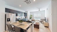 This well-appointed 2-bedroom, 2-bathroom residence is thoughtfully designed with a contemporary aesthetic and efficient use of space across a single floor. The open-concept kitchen, dining, and living area serves as the heart of the home, featuring light hardwood flooring that extends throughout. The kitchen is outfitted with sleek dark cabinetry, granite countertops, stainless steel appliances including a range, microwave, refrigerator, and dishwasher, complemented by a white subway tile backsplash and open shelving. A dining table with seating for four sits adjacent to the kitchen, while the living area offers generous natural light through large windows fitted with blinds and is completed by a ceiling fan. Both bathrooms feature granite-topped white vanities, undermount sinks, matte black fixtures and hardware, and glass-enclosed showers with gray tile surrounds. The primary bedroom offers a comfortable layout with a ceiling fan and wall-mounted climate control unit, while the second bedroom is bright and airy with a large window and hardwood floors. A hallway and closet complete the functional floor plan, making this a well-organized and stylish living space.