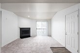 This single-floor residence offers a thoughtfully arranged layout with comfortable living spaces throughout. The living room serves as the heart of the home, anchored by a classic tile-surround fireplace with a clean white mantel. Soft, neutral-toned carpeting extends across the room, complemented by a sliding glass door fitted with vertical blinds that allows natural light to fill the space. A dedicated entryway with hardwood-style flooring provides a welcoming transition into the home.

The layout flows naturally into a dining and secondary living area, separated by a half-wall pass-through that connects to the kitchen. The kitchen is equipped with rich dark wood cabinetry, light-toned countertops, a stainless steel double-basin sink, and a full suite of appliances including a stainless steel refrigerator and an electric range with overhead ventilation. Hardwood-style flooring grounds the kitchen space.

The bedrooms are carpeted and generously sized, each featuring windows with horizontal blinds that frame views of surrounding trees, offering a sense of privacy and connection to the outdoors. Baseboard heating units are present in several rooms for efficient climate control. A bathroom with dark wood vanity cabinetry and light countertops completes the interior. Throughout the home, neutral wall tones and clean finishes create a bright, move-in ready environment.