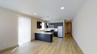Located at 1516 Xavier Street in Denver's vibrant 80204 corridor, this single-floor residence offers a thoughtfully designed open-concept layout that seamlessly blends the kitchen and living areas. The kitchen is a standout feature, showcasing dark espresso cabinetry that contrasts beautifully with light countertops and a central island that provides additional prep space and casual seating. Stainless steel appliances, including a gas range, microwave, and refrigerator, lend a sleek, modern edge to the space. Pendant lighting hangs above the island, complemented by recessed ceiling lights and a track lighting system that ensures the kitchen is well-illuminated throughout the day. Light-toned hardwood-style flooring extends across the living area, adding warmth and continuity to the open floor plan. Large vertical blinds frame a generously sized window, allowing ample natural light to fill the space. A hallway leads to additional rooms beyond the main living area, offering a clear sense of depth and functional flow throughout the unit. The overall ambiance is clean, contemporary, and move-in ready, reflecting the modern residential character of the surrounding Denver neighborhood.