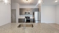 Located at 1332 Holly Rush Ln in Denver, NC, this single-floor home offers a clean, modern aesthetic throughout. The open-concept living and kitchen area is anchored by a granite-topped island with an undermount stainless steel sink, illuminated by stylish pendant lights. The kitchen is equipped with stainless steel appliances—including a refrigerator, range, and microwave—complemented by gray cabinetry and a classic white subway tile backsplash. Light wood-look flooring runs through the main living areas, lending a bright and cohesive feel, while a ceiling fan adds comfort to the living space.

The bedrooms feature soft carpeting and generous closet space, including a walk-in closet with wire shelving for organized storage. Natural light filters in through windows with blinds, enhancing the airy atmosphere of each room.

Both full bathrooms are finished consistently, with granite vanity countertops, gray cabinetry, wood-look tile flooring, and tub/shower combinations clad in white subway tile. Chrome fixtures and towel bars complete the clean, contemporary look.

A dedicated laundry room houses a full-size washer and dryer with overhead wire shelving for added utility. The overall design is cohesive and move-in ready, combining functional layouts with modern finishes throughout.