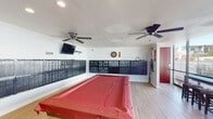 Located at 2039 W Artesia Blvd in Torrance, California, this single-floor community amenity space serves as both a functional mailroom and a casual recreation lounge. The open, well-lit interior features light hardwood-style flooring, recessed ceiling lighting, and crown molding that lend a clean, modern aesthetic throughout.

Dominating the walls are extensive banks of individual metal mailboxes, organized and labeled to serve residents of both 2039 and 2059 addresses. These wall-mounted units span nearly the full perimeter of the room, providing ample mail and package storage for a large residential community.

The recreation area centers around a full-size pool table with a red felt cover, positioned prominently in the open floor plan. A dartboard with scoring accessories and a rack of cue sticks are mounted on the wall, offering additional entertainment options. Two ceiling fans with integrated lights provide comfortable air circulation, while a wall-mounted flat-screen TV adds to the lounge atmosphere.

Large floor-to-ceiling windows and a glass-panel exterior wall on one side of the room flood the space with natural light and offer views of the surrounding outdoor area, where bar-height seating and stools are arranged along the windows—ideal for a relaxed social setting. A red accent door provides a bold pop of color and leads to an adjoining area. Overall, the space balances practical residential services with inviting community recreation amenities.
