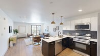 Located at 6515 Ridge Ave in Philadelphia's Roxborough neighborhood, this well-appointed one-bedroom, one-bathroom unit offers a thoughtfully designed open floor plan that maximizes its comfortable footprint. The heart of the home is a striking open-concept kitchen and living area. The kitchen features a two-tone design with crisp white upper cabinets and dark lower cabinetry accented with gold hardware, a slate-toned subway tile backsplash, white quartz countertops, stainless steel appliances, and a central island with seating — all illuminated by a pair of warm brass pendant lights. The living area flows seamlessly from the kitchen and is bathed in natural light from large sliding glass doors that open to a private balcony overlooking the neighborhood streetscape. Hardwood flooring runs throughout the main living areas, adding warmth and continuity. The bedroom is a calm, light-filled retreat with a window offering neighborhood views, hardwood floors, and ample wall space. The bathroom is cleanly finished with light tile flooring, a warm wood vanity with black hardware, and bright vanity lighting. A hallway and closet complete the layout, providing practical storage. The unit's clean lines, modern palette, and quality finishes create a polished, move-in-ready living space.
