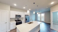This well-designed 1-bedroom, 1-bathroom unit in College Station, Texas, offers a thoughtfully planned single-floor layout with modern finishes throughout. The heart of the home is an open-concept kitchen and living area, where a large center island with a quartz countertop and undermount sink serves as both a prep space and a gathering point. The kitchen is equipped with stainless steel appliances, including a French door refrigerator, electric range, and over-the-range microwave, all complemented by crisp white cabinetry and a tile backsplash. Pendant lighting above the island and recessed ceiling lights add layers of illumination, while dark hardwood-style flooring grounds the space with warmth. The living area extends naturally from the kitchen, featuring a ceiling fan and French doors that invite natural light and outdoor views. An in-unit laundry area with a full-size washer and dryer is conveniently accessible from the kitchen. The bedroom is a comfortable retreat with plush carpeting, a ceiling fan, and a window overlooking greenery. The bathroom features a single-sink vanity, wood-style flooring, and a tiled walk-in shower, with direct access to a spacious walk-in closet, adding excellent storage and convenience to this practical and stylish unit.