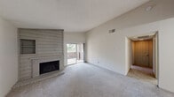 Located in Austin, TX, this two-bedroom, two-bathroom single-floor residence offers a practical and comfortable layout. The living room serves as the heart of the home, highlighted by a wood-paneled fireplace that adds warmth and character, along with a sliding glass door that opens to a private balcony, allowing natural light to fill the space. Soft carpeting extends throughout the living areas and bedrooms, contributing to a cozy atmosphere. A pass-through window connects the living area to the kitchen, enhancing the open feel between spaces. The galley-style kitchen features hardwood-style flooring, black appliances including a refrigerator, range, and microwave, as well as ample cabinetry and counter space along both sides. A hallway leads to the two bedrooms, each carpeted and finished with neutral tones. The primary bedroom is generously sized and includes a walk-in closet with shelving, along with a window that invites natural light. The second bedroom offers a comfortable footprint with closet access. Both bathrooms are cleanly appointed, with one featuring a full tub-shower combination with white tile surround. The textured ceilings and vaulted wall heights in the living area add dimension throughout the home.