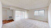 This single-floor residence offers a thoughtfully organized layout encompassing a living area, dining room, kitchen, one bedroom, one bathroom, a hallway, and two closets. The living area is generously sized, featuring neutral-toned carpet, a textured ceiling, and large sliding glass doors flanked by a secondary window that invite natural light and provide outdoor views. A dedicated dining room sits adjacent to the kitchen, which is equipped with warm wood-toned cabinetry, a gas range, dishwasher, refrigerator, and a sink with a window above it—all set on hardwood-style flooring. The spacious primary bedroom is carpeted and features a window with blinds, offering a bright and comfortable retreat. Two closets provide practical storage, one of which is a walk-in style outfitted with built-in shelving and hanging rods. The bathroom includes a full tub-shower combination with clean white tile surround. Throughout the unit, a consistent neutral color palette of whites and beiges creates a calm, cohesive ambiance. A programmable thermostat and smoke detector are also present, adding to the functional nature of this well-maintained residence.