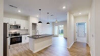 Located at 3025 Headwaters Dr in Southport, NC, this well-designed single-story home offers a thoughtful layout across a compact yet functional floor plan. The open-concept kitchen and living area serves as the heart of the home, featuring light hardwood-style flooring, white shaker cabinetry with matte black hardware, dark granite countertops, a center island with an undermount sink, and stylish pendant lighting. Stainless steel appliances — including a refrigerator, range, and microwave — complete the kitchen, which is finished with a classic subway tile backsplash. The living area flows seamlessly toward a sliding glass door that opens to a private, fenced outdoor patio with artificial turf, ideal for outdoor relaxation. A ceiling fan adds comfort to the living space. The bedroom offers plush carpeting, a ceiling fan, a window with natural light, and access to a dedicated walk-in closet with built-in shelving and hanging rods. The bathroom is clean and bright, featuring a full tub/shower combination with tiled surround, brushed nickel fixtures, and grab bar. A hallway connects all areas efficiently, rounding out this practical and modern home.