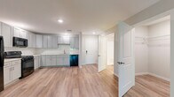 Located at 2800 Commerce Dr in Harrisburg, PA, this single-floor unit offers a thoughtfully designed layout that maximizes its comfortable footprint. The open-concept kitchen and living area serves as the heart of the space, featuring warm wood-tone vinyl plank flooring that flows seamlessly throughout. The kitchen is outfitted with gray shaker-style cabinetry, white subway tile backsplash, light countertops, and a full suite of black appliances including a gas range, over-the-range microwave, refrigerator, and dishwasher. Recessed lighting illuminates the space, adding a clean, modern aesthetic. The living area is bright and open, benefiting from natural light and access to a private balcony through sliding glass doors that frame lush, wooded outdoor views — a tranquil backdrop that enhances the overall ambiance. A dedicated bedroom offers a quiet retreat with neutral tones and continued wood-look flooring. The bathroom is finished with matching gray cabinetry, a white vanity countertop, a mirrored medicine cabinet, and a shower-tub combination. A closet provides practical storage. The unit's cohesive, neutral palette and modern finishes create a clean, move-in-ready environment throughout.