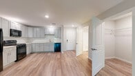 Located at 2800 Commerce Dr in Harrisburg, PA, this single-floor unit offers a thoughtfully designed layout that maximizes its comfortable footprint. The open-concept kitchen and living area serves as the heart of the space, featuring warm wood-tone vinyl plank flooring that flows seamlessly throughout. The kitchen is outfitted with gray shaker-style cabinetry, white subway tile backsplash, light countertops, and a full suite of black appliances including a gas range, over-the-range microwave, refrigerator, and dishwasher. Recessed lighting illuminates the space, adding a clean, modern aesthetic. The living area is bright and open, benefiting from natural light and access to a private balcony through sliding glass doors that frame lush, wooded outdoor views — a tranquil backdrop that enhances the overall ambiance. A dedicated bedroom offers a quiet retreat with neutral tones and continued wood-look flooring. The bathroom is finished with matching gray cabinetry, a white vanity countertop, a mirrored medicine cabinet, and a shower-tub combination. A closet provides practical storage. The unit's cohesive, neutral palette and modern finishes create a clean, move-in-ready environment throughout.