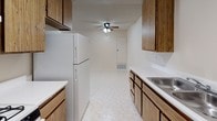 Located at 550 Yucca Ave in Barstow, California, this single-story residence offers a straightforward and functional layout designed for comfortable everyday living. The living area is finished with neutral-toned carpet and features a large window dressed with vertical blinds, allowing natural light to fill the space. A ceiling fan with a light fixture provides both comfort and illumination. The layout flows openly toward the kitchen, which is designed in a galley style with warm wood-toned cabinetry lining both sides, white laminate countertops, a stainless steel sink, and light vinyl flooring. A ceiling fan is also present in the kitchen area, which includes a door providing additional access. The bedrooms are carpeted and finished in neutral tones, each offering closet storage and windows with vertical blinds for light control. The textured ceilings are consistent throughout the living and sleeping areas. Two bathrooms serve the residence: one features a full tub-shower combination with chrome fixtures and tile flooring, while the other includes a vanity with under-sink cabinetry, a large mirror, and overhead lighting. The overall aesthetic is clean and neutral, offering a practical and move-in ready living environment.