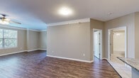 Located at 6771 W 138th Terrace in Overland Park, Kansas, this single-floor residence offers a thoughtfully designed layout with a cohesive blend of modern finishes and practical features throughout. Rich, dark hardwood-style flooring runs through the main living areas and bedrooms, providing a warm and polished aesthetic that complements the neutral taupe wall tones and crisp white trim and crown molding.

The living areas are open and well-proportioned, benefiting from natural light through large windows dressed with white blinds, and ceiling fans that enhance comfort. A private covered balcony accessed via a glass-paneled door extends the living space outdoors, offering views of the landscaped community surroundings.

The kitchen is a functional highlight, featuring dark cabinetry with brushed hardware, stainless steel appliances including a range, microwave, and refrigerator, a classic white subway tile backsplash, and a granite-topped island that provides additional prep and dining space. Light tile flooring grounds the kitchen area distinctly from the rest of the home.

The bedroom includes a spacious walk-in closet outfitted with wire shelving on multiple levels, maximizing storage capacity. The bathroom is finished with a dark-framed vanity mirror, granite countertop, dark cabinetry, and a full tub-shower combination with white tile surround and light tile flooring, presenting a clean and contemporary look throughout.