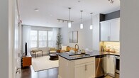 This thoughtfully designed one-bedroom, one-bathroom residence in Lansing, Michigan offers a modern open-concept layout that maximizes every square foot. The combined kitchen and living area serves as the heart of the home, where a sleek kitchen island with a dark granite countertop and undermount sink takes center stage. White shaker cabinetry, a tile backsplash, stainless steel appliances, and stylish pendant lighting complete the kitchen. The living area flows seamlessly from the kitchen, bathed in natural light from large windows dressed with blinds and sheer curtains, creating a bright and welcoming atmosphere. The bedroom is a comfortable retreat, featuring plush carpeting, generous natural light from dual windows with exterior views, and ample room for furnishings. The bathroom mirrors the kitchen's refined aesthetic with white cabinetry, dark granite countertops, a large vanity mirror, and a glass-enclosed shower. A dedicated in-unit laundry area with built-in shelving adds everyday convenience. Polished concrete flooring runs through the main living areas, adding an industrial-modern touch. A glass-paneled entry door connects to an exterior walkway, further enhancing the sense of openness throughout this well-finished residence.