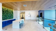 Located at 225 W Olney Rd in Norfolk, Virginia, this thoughtfully designed amenity floor offers a comprehensive suite of communal spaces spread across a generously sized single-story layout. The interior showcases a clean, contemporary aesthetic defined by polished concrete floors, warm wood-paneled ceilings with recessed lighting, crisp white walls, and bold navy blue accent walls that lend the space a cohesive coastal character.

The two living areas are stylishly furnished, featuring plush blue wingback chairs, chartreuse accent seating, built-in shelving, a wall-mounted TV, and a cozy built-in bench nook with decorative lighting. A living green wall and abundant natural light from floor-to-ceiling windows enhance the welcoming atmosphere. The dining area is anchored by a large white island with bar seating, navy cabinetry, a mosaic tile backsplash, and woven pendant lights, creating an inviting kitchen-lounge setting.

A bright dining room with large windows and mobile seating offers a flexible space for gatherings or collaborative use. The fitness center is well-appointed with cardio machines, free weights, weight racks, and full-length mirrors, accompanied by natural light from multiple windows. Glass-railed mezzanine transitions and wide hallways complete this polished, amenity-rich environment.