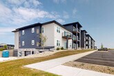 Located at 6556 Stack Dr in Windsor, Wisconsin, this substantial multi-story residential building offers an impressive footprint spanning nearly 18,500 square feet across a single floor plate. The building's exterior showcases a contemporary design, blending dark navy and light gray horizontal lap siding with stone veneer accents at the base, creating a striking and modern aesthetic. Multiple private balconies line the upper levels, providing residents with outdoor space and open views of the surrounding neighborhood and landscape.

The property is set on generously landscaped grounds featuring well-maintained lawns that extend along multiple sides of the building. A paved parking lot with clearly marked stalls runs adjacent to the structure, offering convenient access for residents. Ground-level garage bays with dark panel doors are integrated into the building's base, complemented by a wide concrete apron that provides additional utility and accessibility.

Concrete sidewalks connect the building to the surrounding streetscape, enhancing walkability throughout the site. The neighborhood setting includes open green space and views of nearby residential homes, contributing to a quiet, community-oriented atmosphere. Newly planted trees along the perimeter suggest a commitment to long-term landscaping. The building's design balances functional amenity with modern curb appeal in this growing Windsor community.