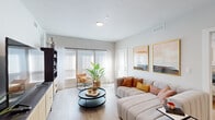 Located at 2700 W Cobalt Dr in Meridian, Idaho, this single-story residence offers a thoughtfully designed, open-concept layout finished with light wood-style flooring, neutral tones, and contemporary details throughout. The living area is generously proportioned, bathed in natural light from large windows fitted with horizontal blinds and a sliding glass door that opens to the outdoors. The space accommodates a sectional sofa arrangement centered around a tiered round coffee table, with a built-in media unit providing ample storage and display space. The kitchen is a standout feature, showcasing two-tone cabinetry — crisp white upper cabinets paired with charcoal lower cabinets — complemented by white quartz countertops, a subway tile backsplash, stainless steel appliances, and a central island with bar seating illuminated by modern pendant lighting. The bedroom offers a comfortable and calm retreat with a window for natural light and easy access to closet space. A flexible secondary room functions well as a home office or den, complete with carpeted flooring and a walk-in closet. The bathroom features a full tub-shower combination with white tile surround and a clean, minimalist vanity. Throughout, the design balances modern functionality with warm, inviting finishes.