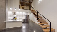 Located in the heart of Minneapolis's North Loop neighborhood, this two-story loft delivers a striking fusion of industrial heritage and modern design. The main level features soaring double-height ceilings with exposed concrete, visible ductwork, and polished concrete floors that anchor the open-plan living and kitchen areas. The kitchen is outfitted with white shaker cabinetry, quartz countertops, a subway tile backsplash, stainless steel appliances including a gas range and French door refrigerator, and a central island. Statement pendant lighting and floor-to-ceiling windows flood the space with natural light and street views, reinforcing the loft's urban character. A sculptural open-tread staircase with a black steel frame, warm wood treads, and cable railings connects the two levels, serving as both a functional and architectural focal point. The upper level features light hardwood flooring, exposed concrete ceilings with industrial piping, and an open railing overlooking the main floor below. Bathrooms are finished with white quartz vanities—including a dual-sink primary bath—tile flooring, and clean, contemporary fixtures. Additional highlights include a spacious walk-in closet with built-in wire shelving around an original concrete column, and a versatile flex room with polished concrete floors. This loft offers a distinctive live-work aesthetic in one of Minneapolis's most dynamic urban neighborhoods.