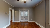 Located in Memphis, TN's 38104 zip code, this single-floor, two-bedroom, one-bathroom unit blends classic architectural character with functional living. Rich hardwood floors flow throughout the main living areas and bedrooms, complemented by crisp white crown molding and baseboards set against neutral gray walls. Ceiling fans are present in multiple rooms, contributing to year-round comfort.

The living area is a standout feature, highlighted by elegant French doors fitted with shuttered blinds that allow for both privacy and natural light. The two bedrooms are well-proportioned, each offering hardwood floors, ceiling fans, and generous window configurations—one bedroom features a triple window arrangement that fills the room with abundant natural light and exterior views.

The kitchen is efficiently laid out with white cabinetry, dark granite-style countertops, a gas range, and a microwave. Tile flooring and a window provide practicality and light. A dedicated area accommodates a full-size refrigerator alongside a stacked washer and dryer unit, offering the convenience of in-unit laundry.

The bathroom retains classic details, including a white pedestal sink, hex-tile flooring, and a full soaking tub with a tiled surround and shower fixture, with a window providing natural ventilation.