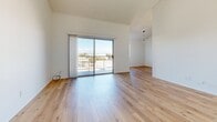 Located at 545 W Sixth St in San Pedro, Los Angeles, this one-bedroom, one-bathroom unit offers a bright and efficiently designed single-floor layout. Light-toned hardwood flooring runs continuously throughout the space, creating a clean, cohesive aesthetic that complements the crisp white walls found in every room.

The open-concept living, dining, and kitchen area serves as the heart of the unit. The living room benefits from soaring vaulted ceilings and a sliding glass door that opens directly onto a private balcony, flooding the space with natural light and offering open views of the surrounding neighborhood. A pendant light fixture marks the transition into the dining area.

The galley-style kitchen is equipped with warm wood cabinetry, tile countertops, a double sink, a dishwasher, and a gas range, providing ample storage and functionality within a compact footprint.

The bedroom is a well-proportioned, sunlit room featuring vaulted ceilings, a large window with natural light, and the same hardwood flooring found throughout. The full bathroom includes a sliding-door shower-tub combination, a vanity with storage, and a small window for ventilation. A hallway and entrance area complete the layout, contributing to a logical and practical flow throughout the unit.