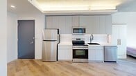 Located at 4720 Third Ave, this modern unit offers four bedrooms and two bathrooms across a thoughtfully designed single-floor layout. The open-concept kitchen is equipped with full-height grey cabinetry, stainless steel appliances including a refrigerator, range, and microwave, complemented by a clean white countertop and an undermount sink. Recessed and cove lighting above the kitchen adds a contemporary touch. Light-toned hardwood flooring runs throughout, unifying the living, dining, and sleeping areas. The living and dining area is bright and airy, featuring exposed concrete ceiling panels that lend an industrial-modern character to the space. Each bedroom benefits from large windows that invite abundant natural light and offer open urban views of the surrounding cityscape. The primary bedroom provides a comfortable footprint with ample room for furnishings. Both bathrooms are finished to a high standard, showcasing floor-to-ceiling marble-patterned wall panels, a soaking tub with an overhead rain showerhead, matte black fixtures, and a white vanity with under-cabinet storage. The overall aesthetic is clean, minimalist, and contemporary, making this a well-appointed urban residence.