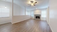 This thoughtfully designed single-floor residence offers a functional and comfortable layout with a range of notable features throughout. The living room serves as the focal point of the home, showcasing a tile-surround fireplace flanked by multiple windows that invite natural light. Wood-look laminate flooring runs throughout the main living areas, complemented by a ceiling fan and a textured ceiling above. The kitchen has been updated with granite countertops, white shaker-style upper cabinets, gray lower cabinets, a classic white subway tile backsplash, and a full suite of stainless steel appliances including a refrigerator, range, microwave, and dishwasher. An adjacent hallway with wood-look flooring connects the kitchen to the rest of the home. The bedrooms feature plush carpeting and vaulted ceilings, with one bedroom offering a sliding glass door with vertical blinds for added natural light. A spacious walk-in closet with wire shelving and hanging rods provides ample storage. The bathroom includes a clean, white tiled tub and shower surround. Carpeted stairs lead to an additional level, and the overall color palette of soft neutrals throughout creates a bright, cohesive ambiance.