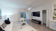 This single-floor residence showcases a thoughtfully designed open-concept layout with a contemporary aesthetic throughout. The kitchen is equipped with stainless steel appliances, including a side-by-side refrigerator, electric range, and built-in microwave, all complemented by sleek dark wood cabinetry and a white quartz island. An in-unit washer and dryer are conveniently tucked into a dedicated laundry alcove nearby.

The living area features wood-style flooring, a ceiling fan, and sliding glass doors that open onto a private balcony, allowing natural light to fill the space and providing outdoor views of surrounding greenery. The room offers generous wall space suitable for large-format artwork or a mounted television.

Multiple bedrooms are finished with plush carpeting, ceiling fans, and windows that bring in natural light. At least one bedroom includes a walk-in closet with built-in shelving. The bathroom presents a clean, white palette with tile surround, a soaking tub and shower combination, a floating vanity, and marble-style flooring.

Overall, the space maintains a modern, neutral tone with crisp white walls and consistent finishes, creating a cohesive and functional living environment.