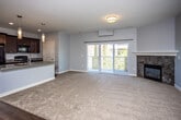 This single-floor residence offers a thoughtfully designed open-concept layout that seamlessly connects the living, dining, and kitchen areas. The living room is anchored by a tile-surround fireplace and a wall-mounted mini-split unit, with plush carpeting underfoot and sliding glass doors that open to a private balcony, allowing natural light to fill the space. A ceiling-height transition from hardwood-style flooring in the kitchen to carpet in the living area creates a clear yet fluid delineation between spaces.

The kitchen is well-equipped with rich, dark espresso cabinetry, granite countertops, black appliances including a refrigerator, range, and built-in microwave, and a central island with a double sink — ideal for both cooking and casual dining.

The bedrooms are carpeted and finished with soft blue-gray walls, white trim, and window blinds. The primary bedroom benefits from dual windows and a ceiling fan, providing excellent natural light and ventilation. Additional bedrooms are similarly appointed with ceiling fans and exterior-facing windows.

Two bathrooms serve the unit: one features a walk-in glass shower with hardwood-style flooring, while the second includes a tub-shower combination with a curved rod, a dark vanity, and matching flooring. The overall aesthetic is clean, modern, and move-in ready.