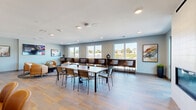Located at 1845 N Water in Milwaukee's vibrant 53212 corridor, this well-appointed amenity space spans a generous single floor designed to serve as a social and recreational hub. The interior is anchored by a bright, open main room featuring light hardwood-style flooring, recessed lighting, and soft blue-gray walls that create a calm, inviting atmosphere throughout.

A central dining area accommodates a large rectangular table surrounded by modern metal-framed chairs, ideal for group gatherings or communal meals. Along the perimeter, a built-in counter with bar-height seating runs beneath a series of large windows, offering seated views of the surrounding Milwaukee neighborhood and filling the space with abundant natural light. A sleek linear fireplace adds warmth and visual interest to one wall.

A dedicated lounge nook features plush cognac leather accent chairs arranged around a round coffee table atop a patterned area rug, accompanied by a wall-mounted flat-screen television and curated artwork — creating a comfortable setting for relaxation or casual viewing. The space is further enhanced by bold, large-format abstract art pieces displayed throughout.

A 3D dollhouse view reveals that the interior connects to a spacious outdoor deck furnished with lounge seating, dining sets, and a fire pit, extending the amenity experience to the outdoors. The overall design reflects a cohesive contemporary aesthetic, balancing functionality and style.
