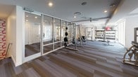 Located at 1270 Spring St NW in Atlanta's vibrant Midtown neighborhood, this fitness center offers a well-appointed, single-floor workout facility designed to support a full range of exercise routines. The space is defined by a clean, contemporary aesthetic, featuring multi-toned striped carpet tiles throughout that add visual depth while providing a practical, durable surface underfoot.

The strength training area is generously equipped, including a cable machine, a power rack with an adjustable bench and weight plates, a leg extension and curl machine, and a dedicated free weights station with a tiered rack stocked with kettlebells and medicine balls. A floor-to-ceiling glass partition wall elegantly divides sections of the facility, creating defined zones while maintaining an open, airy feel and allowing natural light to flow throughout.

The cardio section features a row of treadmills positioned near large windows, filling the area with ample natural light and providing views to the outdoors. A wall-mounted flat-screen television is conveniently positioned for viewing during workouts. Recessed ceiling lighting ensures consistent illumination throughout the space, complemented by subtle tray ceiling detailing that adds an architectural touch. The overall ambiance is modern, functional, and professional, offering a well-rounded environment for fitness and wellness.