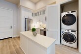 This thoughtfully designed one-bedroom, one-bathroom residence offers a bright and contemporary living experience across a single floor. The open-concept layout seamlessly connects the kitchen, dining area, and living room, creating a fluid and functional space ideal for everyday living and entertaining.

The kitchen is a standout feature, outfitted with full stainless steel appliances including a gas range, built-in microwave, dishwasher, and refrigerator. Crisp white shaker cabinetry extends to the ceiling with glass-front upper panels, complemented by a subway tile backsplash and a white quartz countertop island. A concealed stacked washer and dryer unit adds everyday convenience. Light hardwood flooring runs throughout, tying the spaces together cohesively.

The dining area provides a dedicated space between the kitchen and living room, while the living room impresses with soaring ceilings and floor-to-ceiling windows that flood the space with natural light and frame open city and neighborhood views.

The bedroom is a serene retreat featuring tall windows with outdoor views and a walk-in closet with built-in shelving. The bathroom is finished with white cabinetry, a quartz vanity, an illuminated mirror, and matching light flooring, maintaining the clean, modern aesthetic found throughout the residence.
