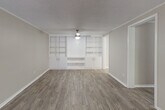 This single-floor residence offers a clean, neutral aesthetic throughout, with warm greige walls, white trim, and a consistent wood-look vinyl plank flooring that flows through the main living areas. The generously sized living room serves as the focal point of the home, highlighted by a striking wall of built-in white shelving and cabinetry that provides both display space and enclosed storage. A ceiling fan anchors the room and ensures comfort year-round. The textured popcorn ceilings add a classic character consistent throughout the space. The kitchen is outfitted with white shaker-style cabinetry, granite-look countertops, and white appliances including an electric range and a full-size refrigerator, delivering a bright and functional cooking environment. The bedroom is a comfortable retreat featuring plush carpet, a ceiling fan with a window that invites natural light and views of surrounding greenery. An ample reach-in closet with dual hanging rods and shelving provides practical storage. The bathroom is cleanly finished with a white vanity, a full tub-shower combination, and consistent wood-look flooring, presenting a fresh and functional space. Overall, this residence combines practical layout with updated finishes for comfortable single-floor living.