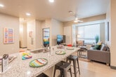 This single-floor unit offers a thoughtfully designed open-concept layout that seamlessly connects the kitchen and living area. The kitchen is equipped with stainless steel appliances, including a range and over-the-range microwave, and features warm wood-toned cabinetry paired with granite countertops. A large central island with a built-in sink provides additional prep space and casual bar seating. The adjacent living area is bright and welcoming, benefiting from large windows with horizontal blinds that allow ample natural light, and is complete with a ceiling fan overhead.

Each bedroom is carpeted and comfortably sized, featuring built-in under-bed storage drawers, a dedicated desk and chair, and large windows that bring in natural light — making them well-suited for both rest and study. Wall art adds a contemporary touch to each room.

The unit includes two bathrooms, each featuring granite-topped vanities with wood-toned cabinetry, light wood-style flooring, and a shared walk-through corridor layout that maximizes privacy and functionality. An in-unit washer is also present, adding everyday convenience. The overall aesthetic is modern and cohesive, with neutral tones, recessed lighting, and clean finishes throughout.