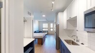 Located at 2829–2879 Fourth St SE in Minneapolis, MN, this modern studio unit offers a thoughtfully designed open-concept layout that efficiently combines living, sleeping, and dining functions in a single, well-organized space. The unit features warm hardwood-style flooring throughout the main area, contrasted by neutral tile in the bathroom, creating a cohesive and contemporary aesthetic.

The kitchen is outfitted with two-tone cabinetry — navy blue lower cabinets paired with crisp white uppers — complemented by white quartz countertops and a classic subway tile backsplash. Stainless steel appliances, including a refrigerator, electric range, and over-the-range microwave, complete the functional cooking space.

The main living and sleeping area is bright and versatile, accommodating a full bed with built-in storage, a compact sofa, and a small coffee table. Large windows along the exterior wall allow ample natural light to fill the room while offering views of the surrounding Minneapolis cityscape. Track lighting overhead provides additional illumination throughout.

The bathroom is finished with large-format gray tile flooring, a navy vanity with a white countertop, and a clean, minimalist design. A separate closet area provides additional storage. The unit's efficient use of space and modern finishes make it a practical and stylish urban living option.