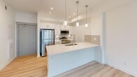 Located in the Nolan Hill community of northwest Calgary, this single-floor, one-bedroom unit offers a well-designed layout that makes efficient use of its compact footprint. The open-concept kitchen and living area serves as the heart of the space, finished with light-toned laminate flooring that runs consistently throughout, contributing to a bright and cohesive aesthetic.

The kitchen is a standout feature, equipped with stainless steel appliances including a refrigerator, electric range, and built-in microwave. White cabinetry extends to the ceiling, maximizing storage, while a neutral tile backsplash adds texture. A peninsula with a white quartz countertop and undermount sink doubles as a breakfast bar, illuminated by a trio of pendant lights overhead. Recessed pot lights provide additional task lighting.

The living area is bright and airy, with large windows and a glass door opening to a balcony that overlooks the surrounding neighbourhood. Baseboard heaters line the perimeter. The bedroom is a comfortable size, also featuring a window with natural light and a dedicated closet nearby for storage.

The bathroom is finished in crisp white, featuring a glass-enclosed shower with tile surround, a white vanity with an integrated sink, and a large mirror. The overall ambiance of the unit is clean, modern, and move-in ready.