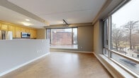 Situated at 100 Trumbull Street within Spectra Park in Hartford, CT, this single-floor residence offers a thoughtfully designed layout with a clean, modern aesthetic throughout. The open-concept living area is anchored by expansive floor-to-ceiling windows that frame views of Hartford's urban streetscape, flooding the space with natural light and creating a bright, airy atmosphere. Light hardwood flooring runs through the main living and kitchen areas, complementing the neutral taupe and gray tones of the walls.

The kitchen features warm honey-toned cabinetry paired with light countertops and a full suite of stainless steel appliances, including a refrigerator, range, and microwave. It opens seamlessly to the living area via a half-wall partition, enhancing the open flow of the space.

Two generously sized bedrooms are finished with soft carpet flooring and windows overlooking the surrounding neighborhood. The space includes two bathrooms — a full bath with a gray vanity, tile countertop, mirror, and a shower/tub combination, and a second accessible bathroom featuring grab bars and coordinating geometric tile flooring. Both bathrooms continue the consistent neutral color palette found throughout the residence, offering a cohesive and functional living environment.