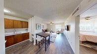 This efficient and thoughtfully designed 1-bedroom, 1-bathroom residence offers a comfortable single-floor layout that maximizes every inch of its footprint. Dark hardwood-style flooring runs throughout, providing a warm and cohesive aesthetic across all living areas.

The open-concept main living area seamlessly connects the kitchen, dining, and living spaces. The kitchen features warm wood cabinetry and is partially separated from the dining area by a structural column with built-in shelving. A compact dining area accommodates a high-top table with seating. The living room is bright and airy, benefiting from a large window that allows generous natural light and exterior views. A ceiling fan with a light fixture provides both comfort and illumination, while a wall-mounted TV adds a modern touch.

The bedroom is a cozy, private retreat with its own ceiling fan, a window with outdoor views, and hardwood-style flooring. The clean, neutral walls offer a calm and restful atmosphere.

The bathroom is clean and functional, featuring a wall-mounted sink, a toilet, and a shower-tub combination with a curtain enclosure. A framed mirror and wood-style tile flooring complete the space.

A hallway connects the rooms, contributing to the unit's practical and efficient flow.