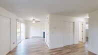 Located at 2875 SW 214th Ave in Hillsboro, Oregon, this single-floor, two-bedroom, one-bathroom home offers a clean and functional layout with consistent light wood-style flooring throughout. The open living and dining area is bright and welcoming, featuring a ceiling fan with light fixture, a baseboard heater, and a sliding glass door that invites natural light and provides views of the surrounding greenery. The kitchen flows directly off the living area and is outfitted with two-tone cabinetry — white upper cabinets with brushed nickel hardware and navy lower cabinets — complemented by light countertops, a stainless steel sink, and white appliances. Both bedrooms are well-proportioned, bathed in natural light from windows overlooking mature trees, and each includes its own closet with hanging rod. The unit features an abundance of closet storage, with six closets spread throughout the floor plan. The bathroom includes a full tub-shower combination with a clean white surround, a vanity with light countertop, and tile flooring. Textured ceilings and bright white walls are consistent throughout, giving the home a fresh, move-in-ready feel. A connecting hallway ties all rooms together in a practical and efficient layout.