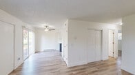 Located at 2875 SW 214th Ave in Hillsboro, Oregon, this single-floor, two-bedroom, one-bathroom home offers a clean and functional layout with consistent light wood-style flooring throughout. The open living and dining area is bright and welcoming, featuring a ceiling fan with light fixture, a baseboard heater, and a sliding glass door that invites natural light and provides views of the surrounding greenery. The kitchen flows directly off the living area and is outfitted with two-tone cabinetry — white upper cabinets with brushed nickel hardware and navy lower cabinets — complemented by light countertops, a stainless steel sink, and white appliances. Both bedrooms are well-proportioned, bathed in natural light from windows overlooking mature trees, and each includes its own closet with hanging rod. The unit features an abundance of closet storage, with six closets spread throughout the floor plan. The bathroom includes a full tub-shower combination with a clean white surround, a vanity with light countertop, and tile flooring. Textured ceilings and bright white walls are consistent throughout, giving the home a fresh, move-in-ready feel. A connecting hallway ties all rooms together in a practical and efficient layout.