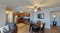 This single-floor unit offers a thoughtfully designed layout connecting the main living areas in a cohesive, functional flow. The kitchen is well-equipped with warm honey-toned cabinetry, dark countertops, and a full suite of stainless steel appliances, including a refrigerator, dishwasher, and range. A neutral tile-patterned area rug anchors the space, which transitions seamlessly into the adjacent dining area. The dining room features crown molding, a ceiling fan with a light fixture, and wood-look flooring that carries throughout the unit, lending warmth and continuity. A framed mirror accents the wall, enhancing the sense of space.

The living room receives natural light through large windows with views of the surrounding greenery, and includes baseboard heating and a wall-mounted air conditioning unit. Crown molding adds a polished finishing touch throughout the common areas.

Both bedrooms are comfortably sized, featuring wood-look flooring, crown molding, natural light from windows, and baseboard heating. The primary bathroom includes a tub-shower combination, while the second bathroom offers a clean, minimalist design with a vanity and tile flooring. Together, these spaces create a practical and comfortable living environment.