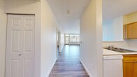 Located at 431 NW 100th Pl in Seattle, WA, this one-bedroom, one-bathroom unit offers a well-organized layout with consistent light wood-style flooring running throughout every room. The open living area is a standout, featuring large windows and a glass balcony door that flood the space with natural light and provide views of the surrounding Seattle neighborhood. The adjoining kitchen is efficiently designed in a U-shape with warm honey-toned cabinetry, white appliances including a refrigerator, electric range, and dishwasher, a double sink, and a pass-through counter that connects to the living area. The bedroom is a comfortable, private retreat with a window offering additional natural light and neighborhood views, a spacious double-door closet, and a baseboard heater. The bathroom features a wide vanity with dual mirrors, warm wood cabinetry, and a clean white countertop, conveniently positioned adjacent to both the bedroom and the kitchen. A hallway connects the main living spaces and provides access to all rooms. The unit's neutral wall tones, clean lines, and consistent flooring give it a bright, cohesive feel throughout.