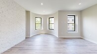 Located at 6-12 Blackwood Street in Boston's Fenway neighborhood, this thoughtfully designed studio offers a bright and modern living experience. The open living area is anchored by a striking exposed white brick accent wall that adds character and warmth, while light-toned hardwood flooring runs throughout, enhancing the sense of space. A distinctive curved architectural detail frames a trio of black-trimmed windows, filling the room with natural light and offering views of the surrounding neighborhood. A wall-mounted mini-split unit provides efficient climate control.

The kitchen is well-appointed with two-tone cabinetry — white upper shaker-style cabinets and gray lower cabinets — paired with crisp white countertops and a full suite of stainless steel appliances, including a gas range, built-in microwave, and refrigerator. Recessed lighting illuminates the space throughout.

The bathroom is finished to a high standard, featuring large-format marble-look wall tiles in the walk-in glass-enclosed shower, gray floor tiles, a vanity with an undermount sink, and clean, modern fixtures. A dedicated closet rounds out the functional layout, making this a well-organized and stylish urban residence.