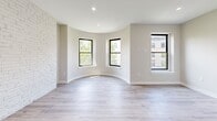 Located at 6-12 Blackwood Street in Boston's Fenway neighborhood, this thoughtfully designed studio offers a bright and modern living experience. The open living area is anchored by a striking exposed white brick accent wall that adds character and warmth, while light-toned hardwood flooring runs throughout, enhancing the sense of space. A distinctive curved architectural detail frames a trio of black-trimmed windows, filling the room with natural light and offering views of the surrounding neighborhood. A wall-mounted mini-split unit provides efficient climate control.

The kitchen is well-appointed with two-tone cabinetry — white upper shaker-style cabinets and gray lower cabinets — paired with crisp white countertops and a full suite of stainless steel appliances, including a gas range, built-in microwave, and refrigerator. Recessed lighting illuminates the space throughout.

The bathroom is finished to a high standard, featuring large-format marble-look wall tiles in the walk-in glass-enclosed shower, gray floor tiles, a vanity with an undermount sink, and clean, modern fixtures. A dedicated closet rounds out the functional layout, making this a well-organized and stylish urban residence.