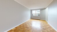 Located on the 7th floor at 130 Jameson Ave in Toronto's Parkdale neighbourhood, this one-bedroom, one-bathroom unit offers a functional and well-appointed layout across a single floor. The main living area is notably spacious for a one-bedroom unit, featuring classic parquet wood flooring in a basket-weave pattern that adds warmth and character throughout. Soft grey walls and crisp white crown moulding provide a clean, neutral backdrop, while a large window floods the room with natural light and offers outward views. A traditional cast-iron radiator sits beneath the window, providing efficient heating. The compact kitchen is efficiently designed with white shaker-style cabinetry, grey countertops, light tile flooring, and stainless steel appliances including a full-size refrigerator and stove. The hallway connects the living space to the bedroom and bathroom, maintaining a logical and comfortable flow. The bathroom features full white subway tile surrounding a bathtub and shower combination, a pedestal-style vanity with a mirrored medicine cabinet, and chrome fixtures. The entry area continues the parquet flooring and leads seamlessly into the main living space, completing a cohesive and practical unit.