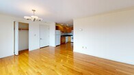 Located at 100 Jersey St in Boston's Fenway neighborhood, this single-floor residence offers a well-designed layout with a variety of functional spaces. The open living area is a standout feature, showcasing gleaming hardwood floors, large windows that frame striking views of the Boston skyline, and a stylish chandelier overhead that adds warmth to the room. Natural light flows generously throughout, creating a bright and welcoming atmosphere.

The kitchen is thoughtfully appointed with warm honey-toned wood cabinetry, dark granite countertops, a stainless steel sink, and white appliances including a dishwasher, refrigerator, and range. Recessed lighting and a wine rack accent add to its inviting character. The kitchen flows seamlessly into the living area, making the space ideal for entertaining.

The bedrooms are carpeted for comfort, each offering ample closet space with built-in hanging rods — one features a double-door closet, while the other has an open-style closet alcove. Both rooms are finished in soft neutral tones.

The full bathroom is well-equipped with a tub-shower combination, a wood vanity with dark countertop, a mirrored medicine cabinet, tile flooring, and a bright vanity light. The overall ambiance of the residence is clean, functional, and well-lit throughout.