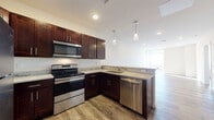 Located at 14650 Detroit Ave in Lakewood, Ohio, this well-appointed single-floor unit offers a thoughtfully designed layout with contemporary finishes throughout. The kitchen serves as a standout feature, showcasing rich dark wood cabinetry with sleek hardware, light granite countertops, and a full suite of stainless steel appliances including a range, over-the-range microwave, dishwasher, and refrigerator. Pendant lighting over the peninsula adds a refined touch, while the open sightline to the living area creates a welcoming, connected flow. Wood-style plank flooring runs throughout the main living spaces, providing warmth and visual continuity. The living area is generously sized, bathed in natural light from large windows, and features recessed lighting for added brightness. The bedroom offers a bright, open feel with the same wood-style flooring and access to a spacious walk-in closet outfitted with wire shelving systems for organized storage. The bathroom is finished with a granite-topped dark vanity, a large mirror, tile flooring, and a full tub/shower combination. The overall design palette of neutral walls, dark cabinetry, and natural-toned flooring creates a clean, modern ambiance throughout the space.