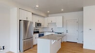 This two-story space offers a thoughtfully designed layout across two floors, with the upper level providing the majority of the living area. The interior embraces a clean, contemporary aesthetic throughout, characterized by neutral white walls, light hardwood-style flooring on the main level, and plush carpeting in the upper-floor rooms.

The kitchen is a standout feature, showcasing crisp white shaker-style cabinetry extending to the ceiling, a classic white subway tile backsplash, and a full suite of stainless steel appliances including a refrigerator, range, microwave, and dishwasher. A central island with a dark countertop provides additional workspace and seating, anchoring the kitchen as a functional hub.

Living areas benefit from generous natural light, with multiple windows offering outdoor views. Recessed lighting and ceiling fans are present throughout, ensuring well-lit, comfortable spaces. The bathroom features white cabinetry with dark hardware, a gray countertop, and a tub-shower combination. A walk-in closet with built-in shelving and hanging rods offers practical storage. The overall ambiance is fresh, clean, and move-in ready.