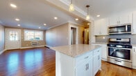 Located at 1 Kowal St in Clifton, NJ, this single-floor residence offers a thoughtfully designed layout with a clean, modern aesthetic carried consistently throughout. The kitchen serves as a central highlight, showcasing white shaker cabinetry, gray subway tile backsplash, and granite countertops that extend across both the perimeter surfaces and a generous central island. Stainless steel appliances — including a gas range, microwave, dishwasher, and refrigerator — complement the crisp, contemporary finish. Pendant lighting above the island and recessed lighting above add warmth and functionality to the space. Rich hardwood flooring flows seamlessly from the kitchen into the open living areas, which feature elegant crown molding and neutral-toned walls that create a welcoming ambiance. Natural light pours in through multiple windows, offering views of the surrounding neighborhood. The living and bedroom areas are spacious and versatile, each equipped with wall-unit HVAC systems and baseboard heating for year-round comfort. The bathroom is finished with neutral tile flooring, a tiled tub-and-shower surround with decorative accent tile, and a vanity with ample counter space. A dedicated entry door with glass panel detailing provides a bright, welcoming entrance to the home.